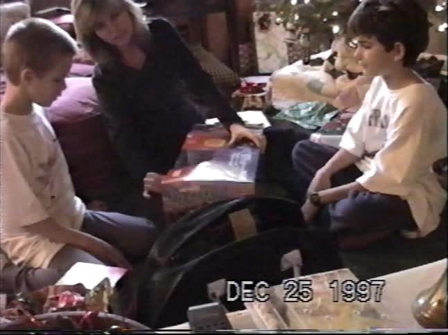 Vintage home video from 1997 shows two young boys opening Christmas presents together by the tree