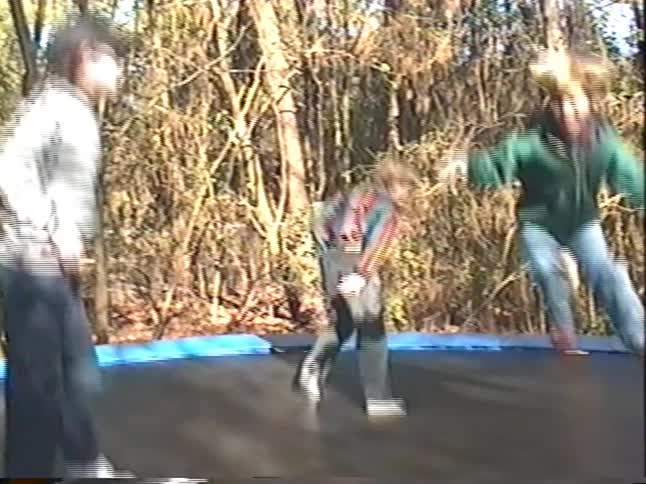 Vintage VHS footage captures three exuberant boys joyfully jumping on a backyard trampoline