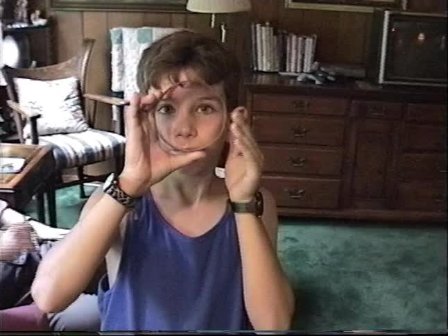 A young boy plays with a slinky toy, looking at the camera in a grainy, vintage home video