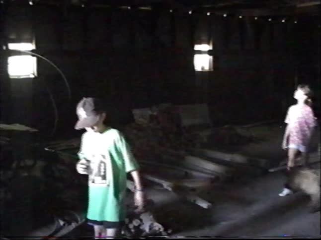 Vintage home movie footage shows kids and a dog exploring the dark, debris-filled interior of an old building