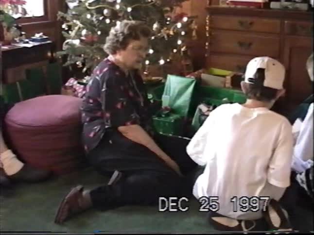 A grandmother and her two grandsons sit on the floor by the Christmas tree opening presents on Christmas morning in 1997