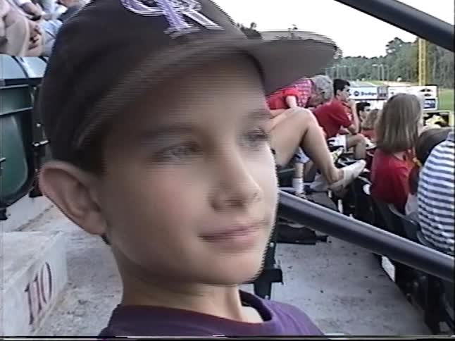Close-up shot from a 1997 home video of a young boy smiling in the stands at a baseball game
