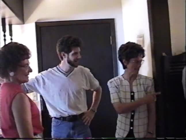 A man and two women stand in a hallway having a pleasant conversation in this archival home video