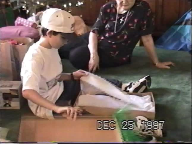 A young boy unwraps a large present on Christmas morning as his grandmother watches in this 1997 home movie