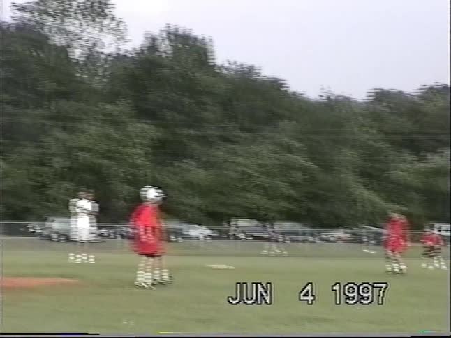 A young boy hits the ball and runs to first base during a little league baseball game, captured on home video in 1997