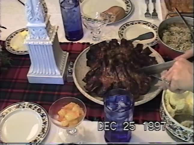 Vintage VHS footage from Christmas 1997 shows a festive dinner table as a crown roast is carved for the family meal