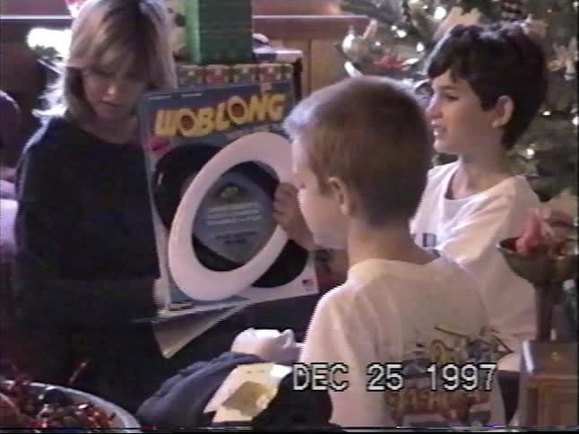 Vintage VHS footage from 1997 shows two young boys opening a board game gift on Christmas morning next to the tree