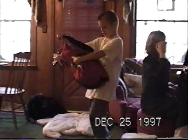Vintage VHS footage shows a young boy excitedly unwrapping a new red duffel bag on Christmas morning in 1997