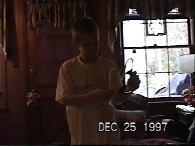 Vintage VHS footage from Christmas 1997 shows a young boy aiming his new toy slingshot indoors