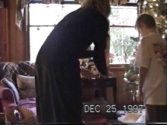 A 1997 home video shows children and their mother opening presents by the Christmas tree