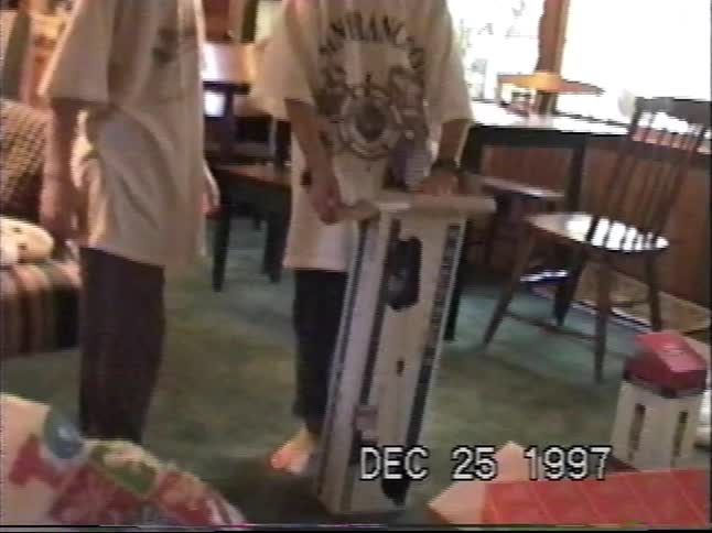 Siblings gather around the Christmas tree to open a large, exciting present in a nostalgic 1997 home video