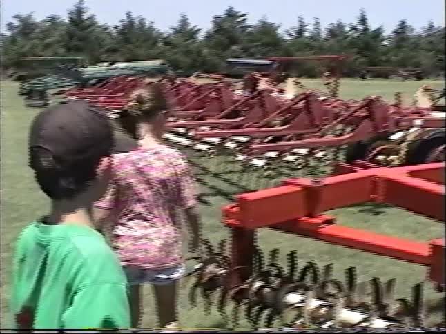 Vintage 1990s VHS footage shows children inspecting large red farming equipment at a rural auction
