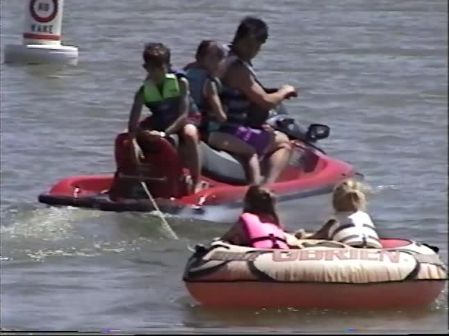 Vintage home video captures a fun family day on the lake, with a father towing his kids in an inflatable tube behind a jet ski