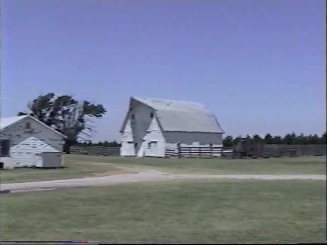 Children discover a small toad in the grass on a farm, followed by a panoramic view of the rural property with its barns, silo, and tractor