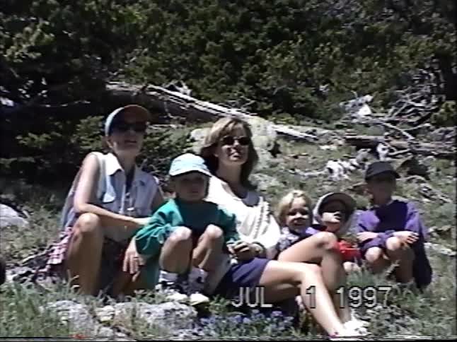 A slow zoom on a group of women and children posing together for a home video on a sunny day in the mountains in 1997