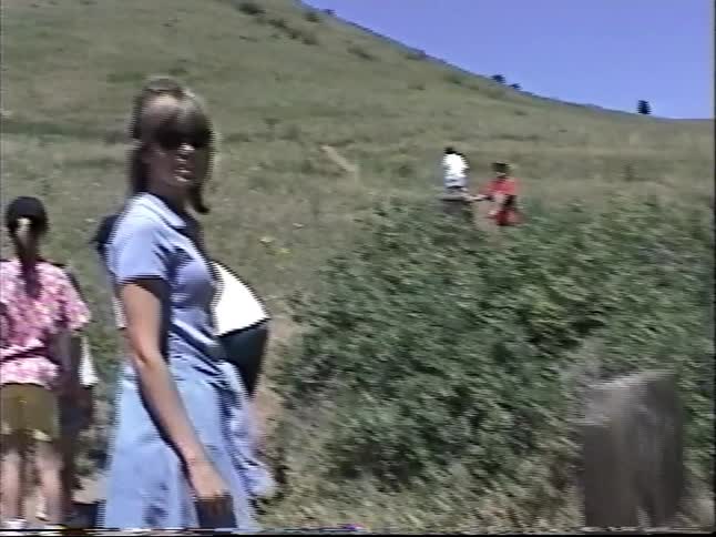 Vintage home video footage of a family hiking up a beautiful grassy hill on a bright sunny day