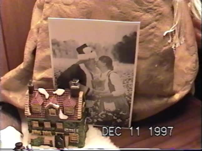 A nostalgic home video from 1997 shows a close-up pan of a charming Christmas village display with lighted houses and figurines