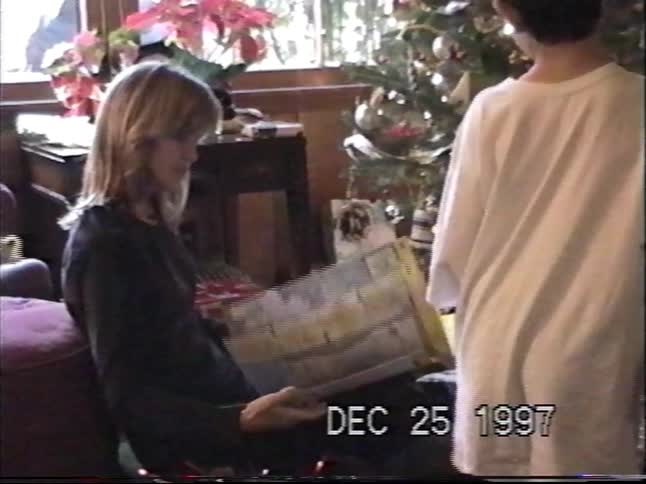 Vintage home video of a family gathered around the Christmas tree opening presents together on Christmas morning in 1997