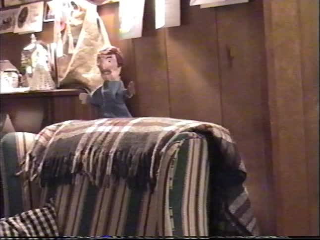 A mustached hand puppet sits on the back of a couch before a young boy comes to play with it in this vintage home video
