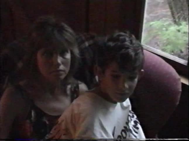 A grainy VHS home video from 1997 shows a family sitting together on a couch in a dimly lit living room