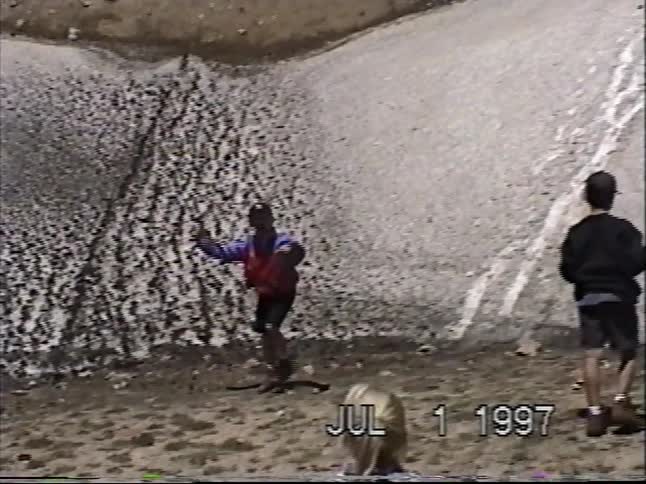 Vintage VHS footage from 1997 shows a family having fun sliding down a patch of dirty snow in the mountains during the summer