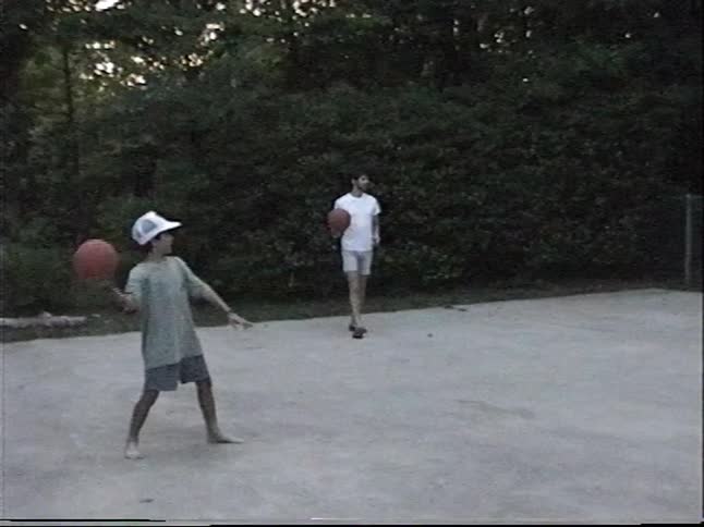 A father and his two young sons play basketball together on a concrete court in their backyard