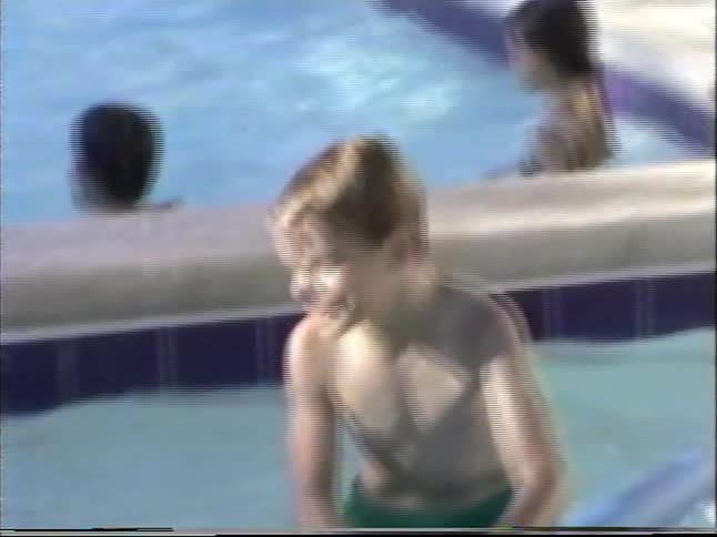 Vintage footage of a diverse group of children swimming and playing with pool noodles and balls in a community swimming pool