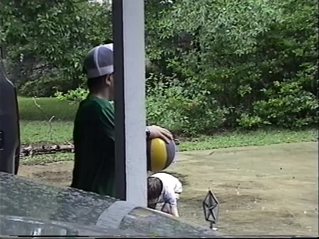 Vintage footage shows a group of kids joyfully playing basketball and with water guns on a flooded driveway during a rainstorm