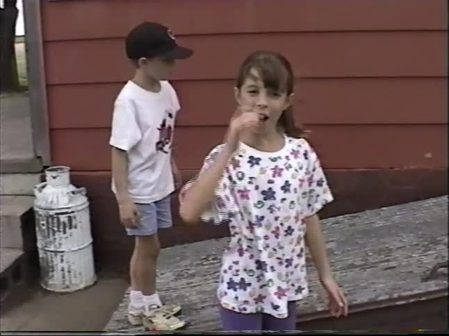 Three nostalgic children from the 1990s play together in the backyard, opening an old wooden cellar door on a summer day