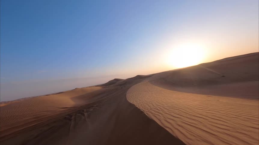 An FPV drone captures a breathtaking flight over expansive desert sand dunes during a beautiful sunrise