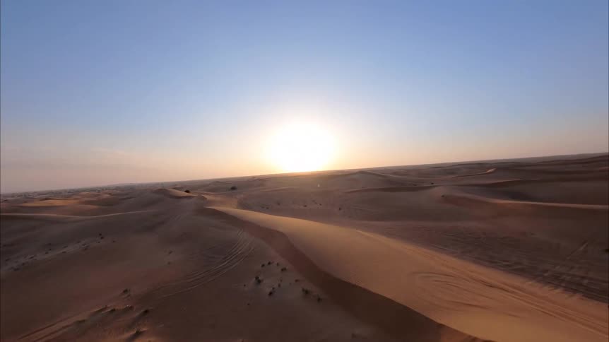 Majestic aerial footage captures the endless golden sand dunes of a desert as the sun sets on the horizon