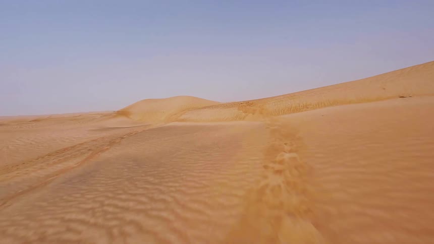 A fast-paced first-person view drone flight soars low over the vast and empty golden sand dunes of a desert