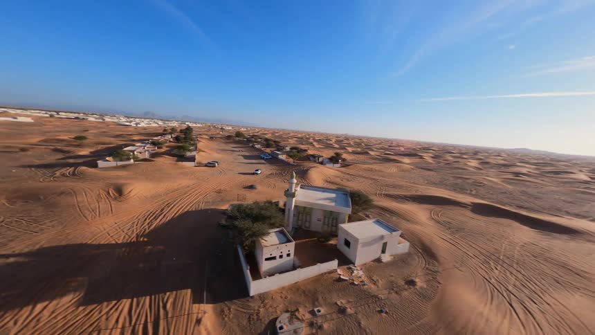 An FPV drone captures a stunning aerial view as it flies over a vast desert and descends upon an abandoned village and mosque being reclaimed by sand dunes