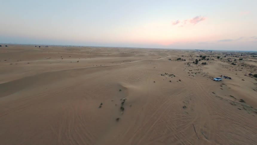Aerial FPV drone footage flies over a modern architectural building and out into the vast desert landscape at sunset