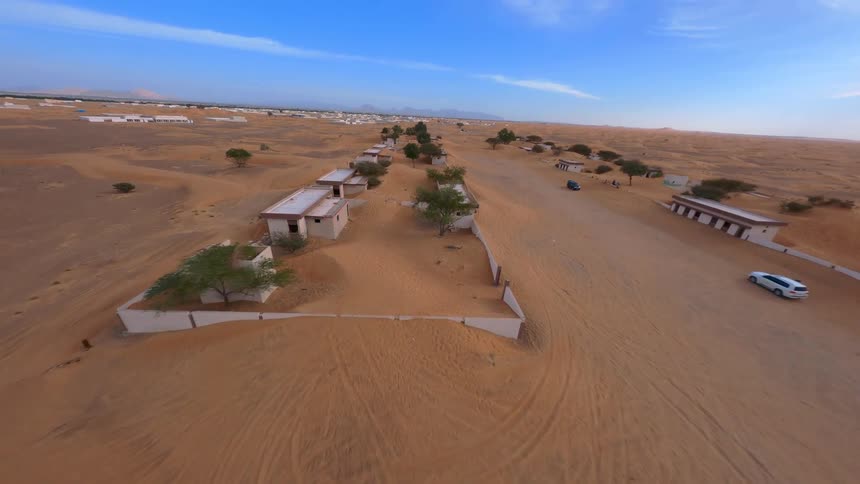 An FPV drone flies over a deserted mosque and abandoned village slowly being reclaimed by the vast orange desert sands