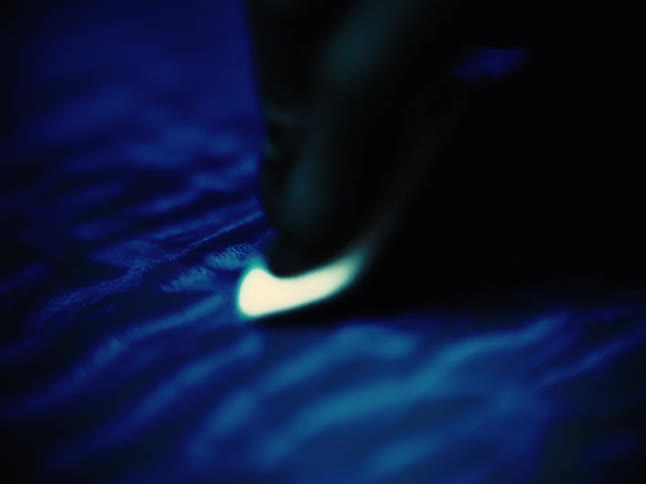 Abstract macro shot of a luminous tip moving across a dark, rippling blue texture