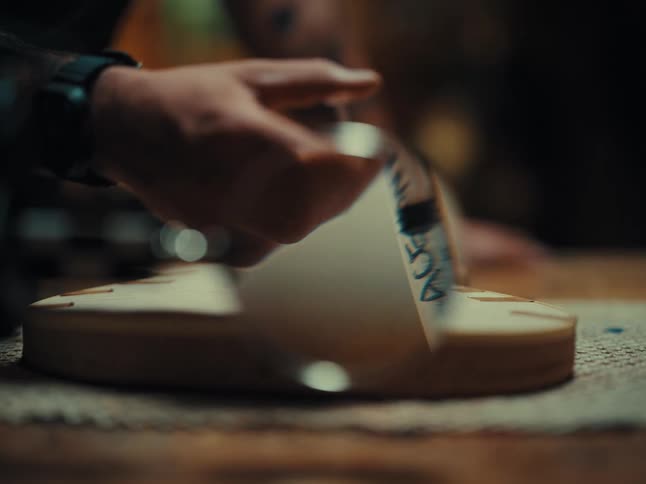 Skilled artisan meticulously injects adhesive with a syringe into the wooden body of a custom-built guitar in a dimly lit workshop