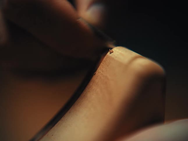An artisan meticulously carves and files the edge of a piece of wood in a dark workshop, captured in a detailed macro shot