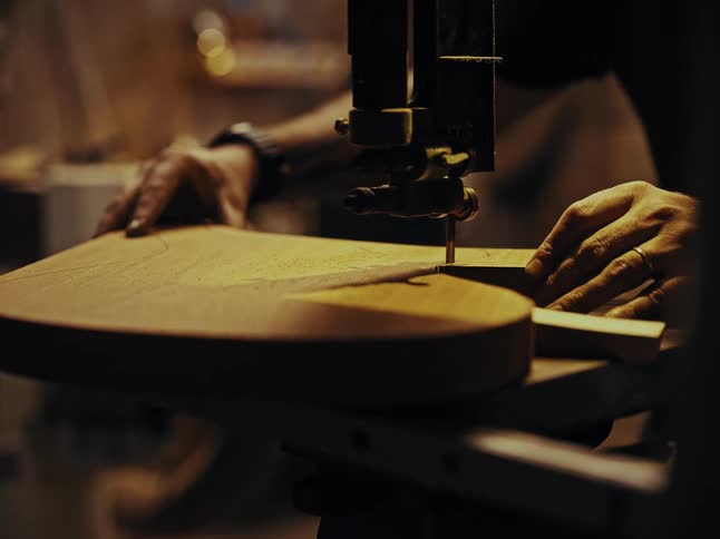 A skilled luthier carefully uses a band saw to cut the intricate shape of a guitar body in their workshop