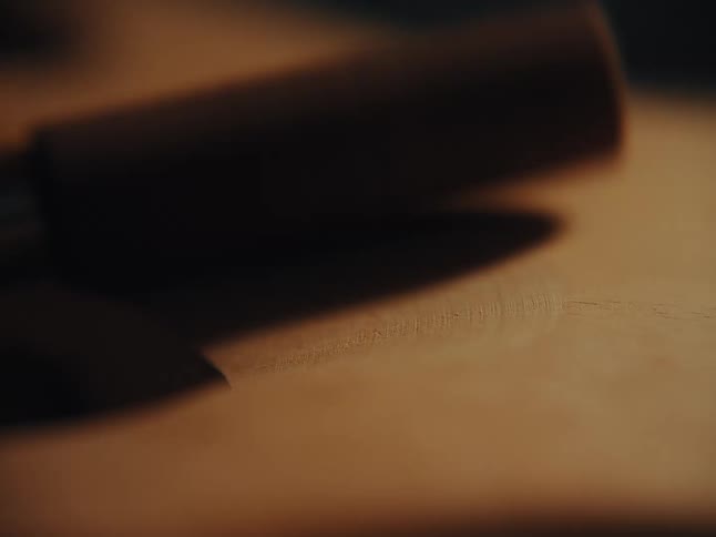 An abstract, out-of-focus macro shot of a tool handle resting on a wooden surface in warm, low light