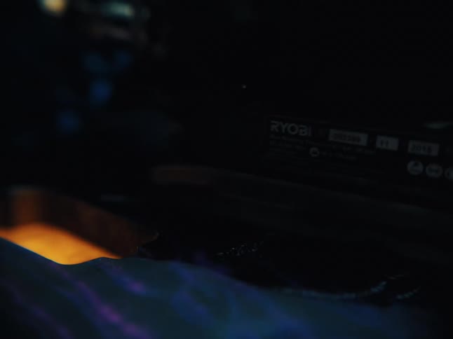 Macro view of a vibrating power sander moving across a dark surface in a moody, dimly lit workshop