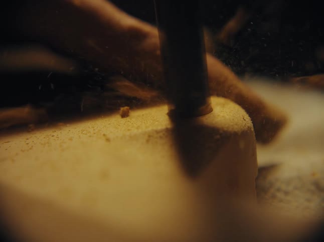 Slow-motion macro shot of a drill boring a hole into a piece of wood, with sawdust flying everywhere