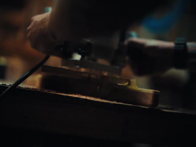 Close up of a craftsman using a power router to carve a piece of wood, sending sawdust flying in slow motion