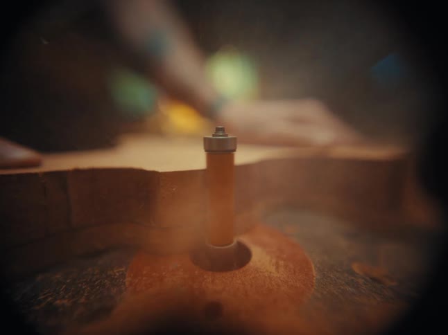 Macro slow motion shot of a router bit spinning and cutting the body of a guitar in a luthier's workshop