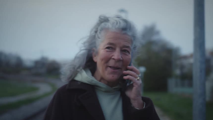 A close-up of a happy senior woman with grey hair laughing while on a phone call at a train station