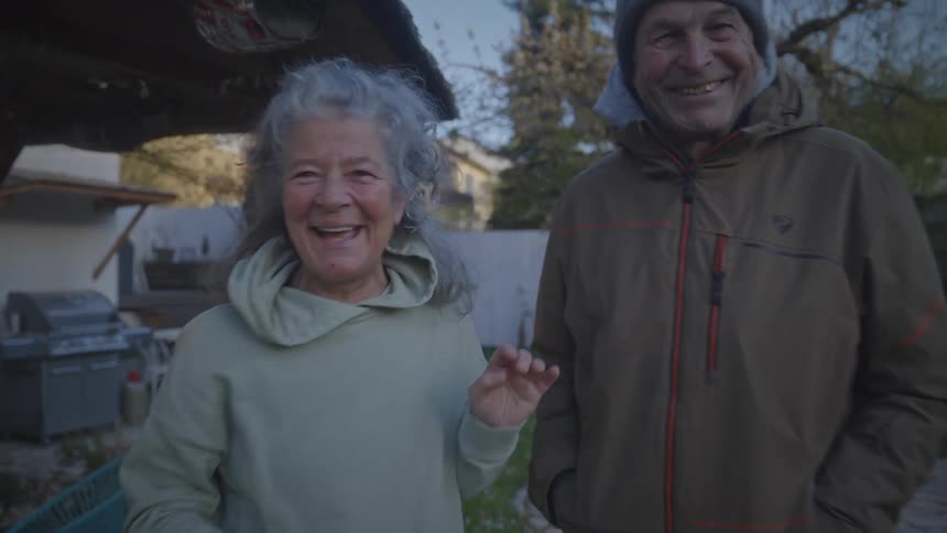 A joyful elderly couple shares a laugh in their backyard in a heartwarming slow-motion shot