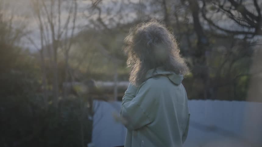 Backlit by the golden hour sun, a mature woman answers her cell phone in a peaceful backyard garden
