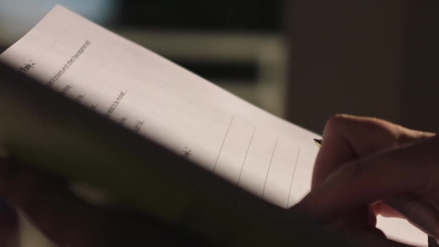Close-up of a person's hand writing and reviewing notes on a document with a pen