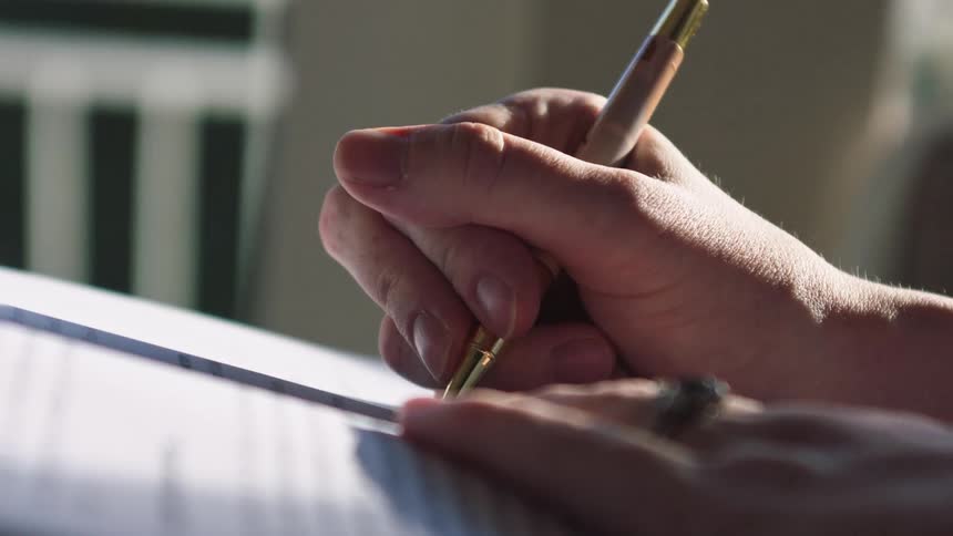 Close up slow motion shot of a hand with a pen writing on a piece of paper in the sunlight
