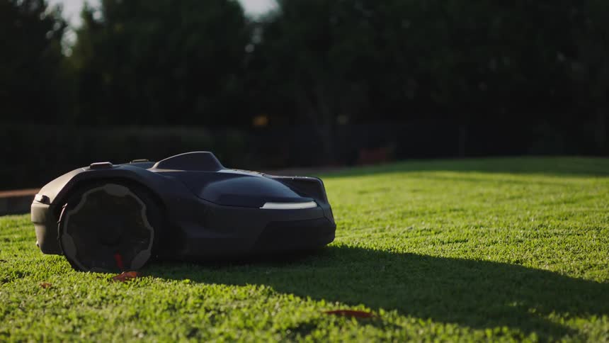 A sleek, black robotic lawnmower glides effortlessly across a lush green lawn, autonomously maintaining the yard in the warm afternoon sun